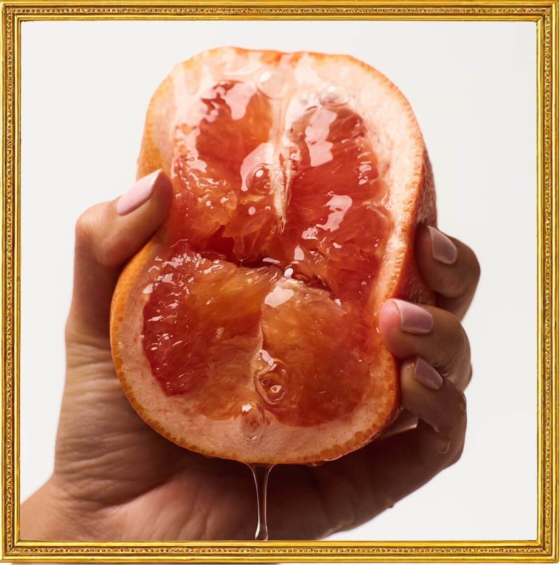 Hand holding a halved grapefruit dripping with lubricant in a gold frame